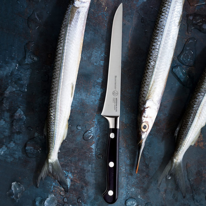 6 inch boning knife next to 3 sardines on a blue and copper surface with water drops
