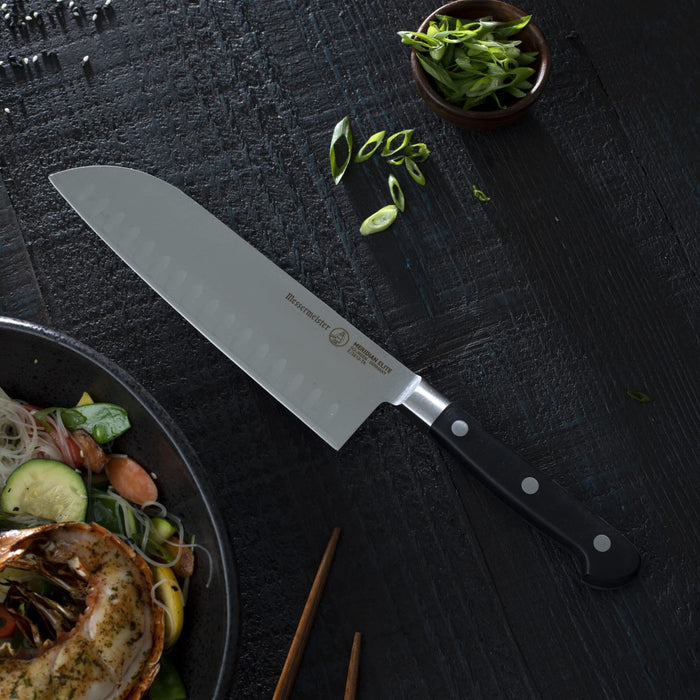 7 inch santoku knife next an assortment of greens on a black surface