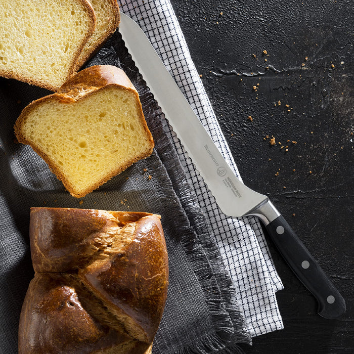 8 inch bread knife next to a loaf of bread on napkins placed on a black surface