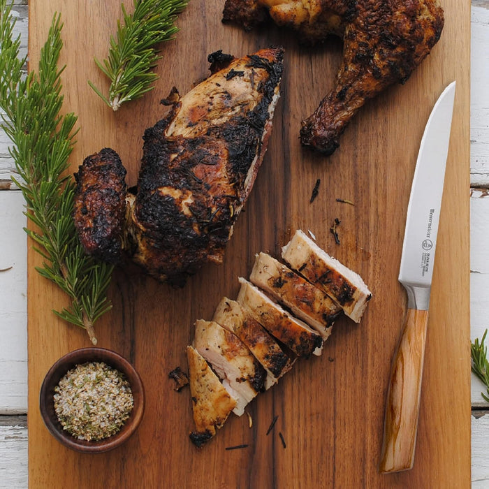 Sliced grilled chicken on a wooden cutting board with rosemary and a knife.