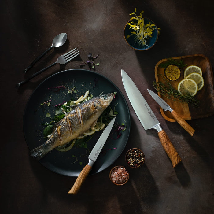 3 knives, silver, and plates filled with fish, vegetables, and lemons on a metal type surface