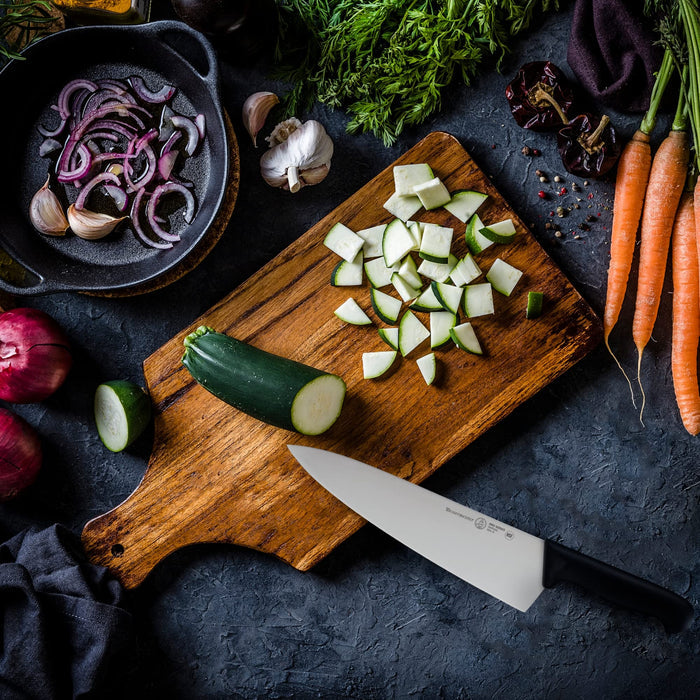 10 inch chef knife next to an assortment of vegetables on a cutting board and a black surface