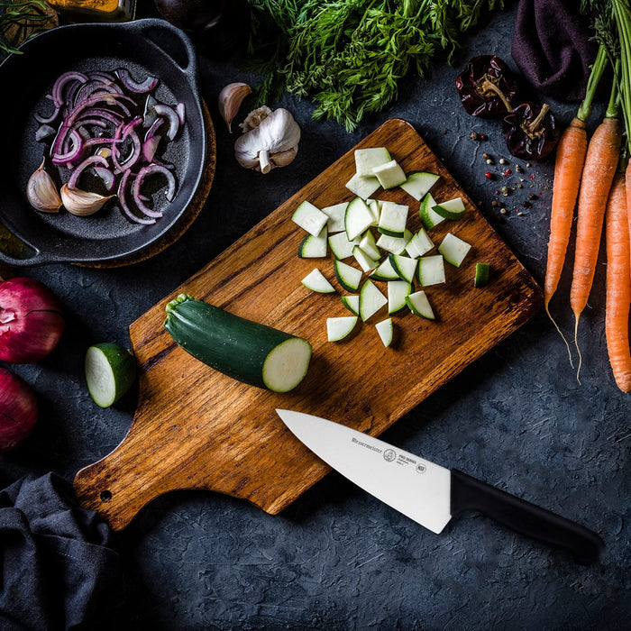 6 inch chef knife next to an assortment of vegetables on a cutting board and black surface