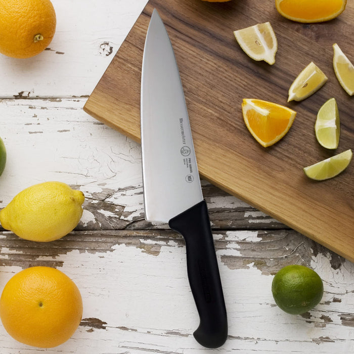 8 inch chef knife next to lemons and limes on a wooden cutting board a white wooden surface