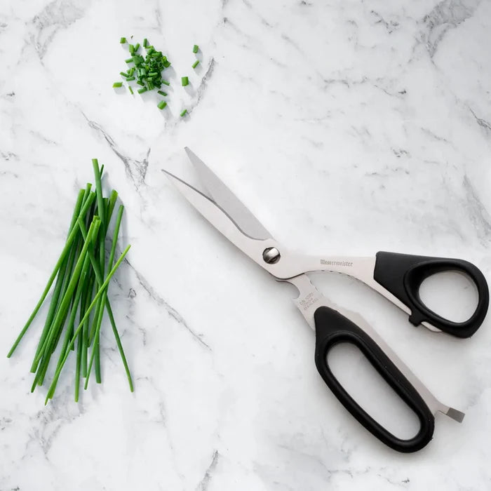 Scissors with black handles on a marble surface next to chopped green herbs
