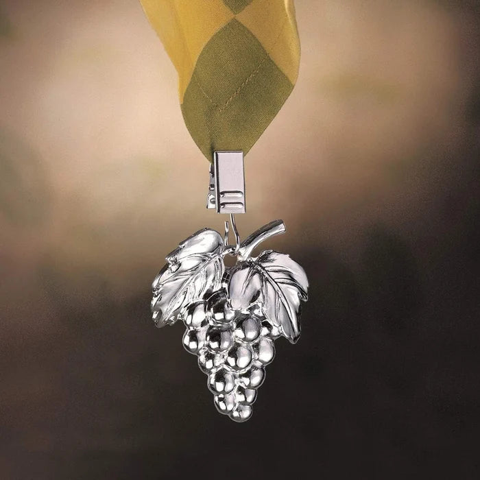 A silver metal grape cluster pendant hanging from a green and yellow striped ribbon, set against a dark, softly blurred background.