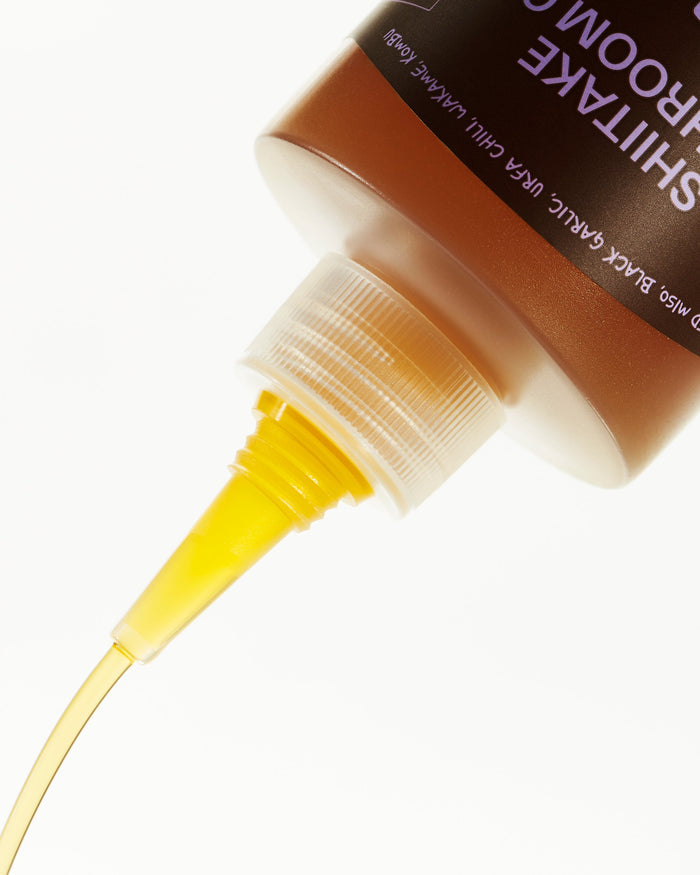 Close-up of a bottle with a yellow liquid being poured, on a white background.