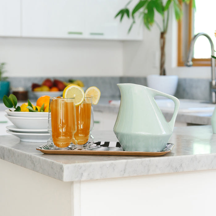 Two glasses of iced tea with lemon slices on a kitchen counter, accompanied by a sage green pitcher.