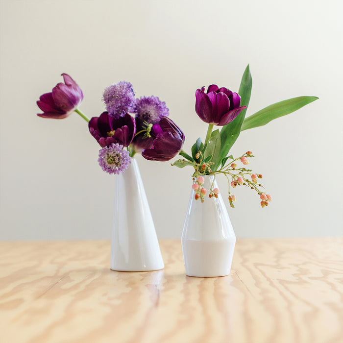 Two white vases with purple flowers on a wooden surface