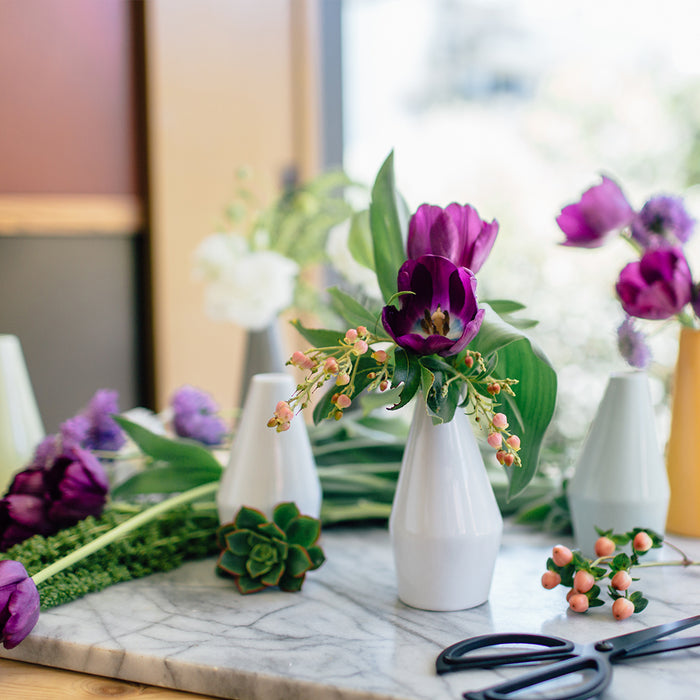 Decorative setting with white vases, purple tulips, and greenery on a marble surface.