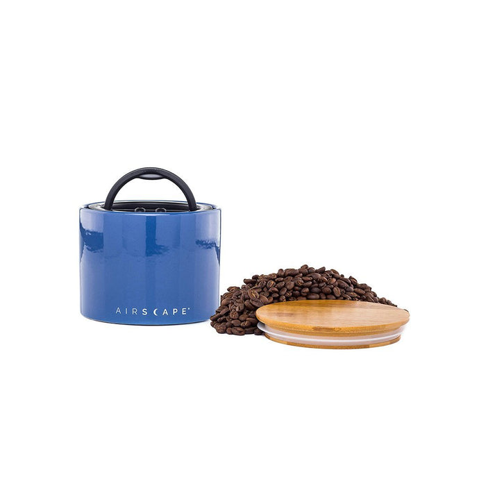 Blue air tight container with black handle and lid, with coffee beans on a white background.
