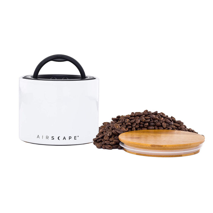 White air tight container with black handle and lid, with coffee beans on a white background.