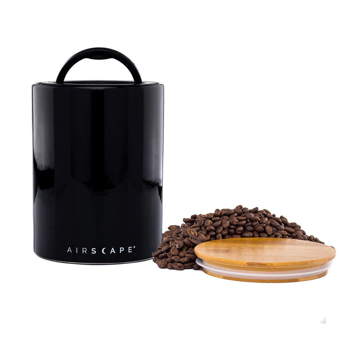Black air tight container with black handle and lid, with coffee beans on a white background.
