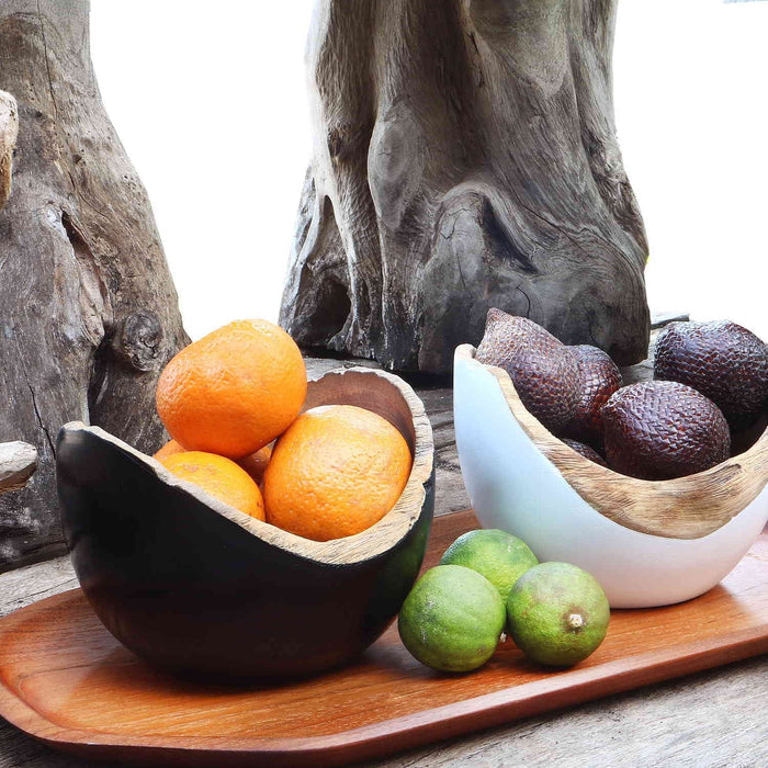 2 Rico & Plato bowl with black exterior and oranges inside and another with white exterior with fruit inside placed on a wooden plate outside