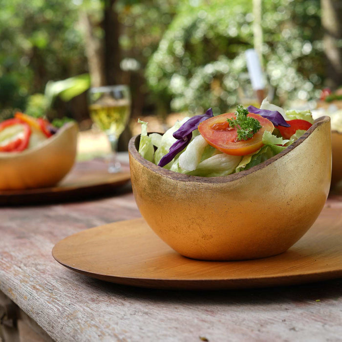 Rico & Plato adagio teak bowl with gold leaf exterior with a salad inside placed on a wooden table outside