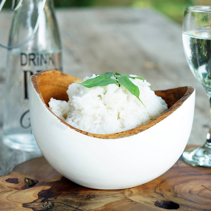 Rico & Plato adagio teak bowl with white exterior and rice inside next to glasses of water displayed on a wooden surface outside