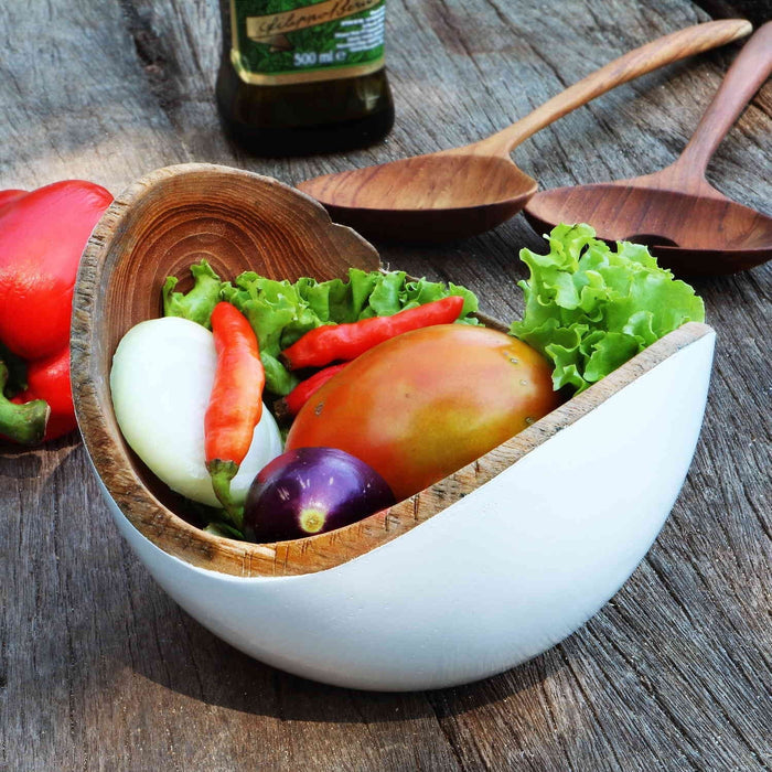 Rico & Plato adagio teak bowl with white exterior and vegetables inside next to oil and salad servers on a wooden surface