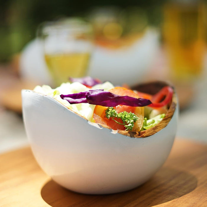Rico & Plato adagio teak bowl with white exterior with a salad inside on a wooden surface outside
