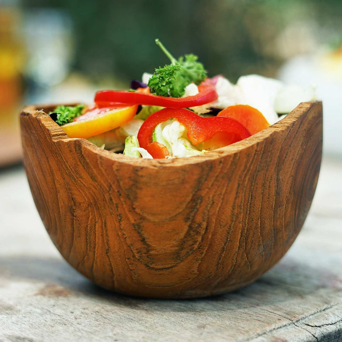 Wooden bowl filled with a salad on a wooden surface outside