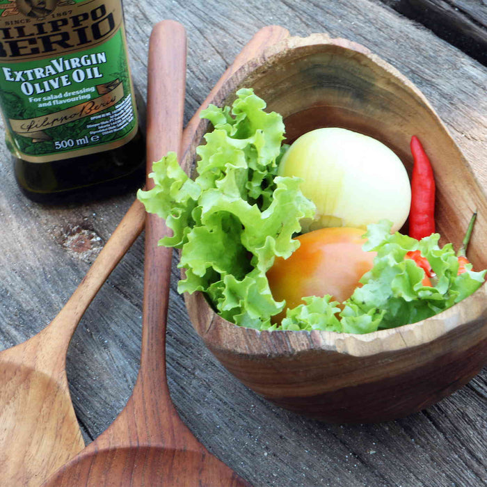 Rico & Plato adagio teak bowl with vegetables inside next to oil and salad server on a wooden surface