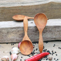 A set of three wooden spoons with a golden-brown hue, displayed on a wooden surface surrounded by spices, garlic, and a red chili.