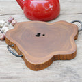 Rico & Plato amla teak trivet with iron handles next to garlic, shallots, peppercorns, and a red kettle on a wooden surface