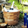 Rico & Plato angelia teak wine champagne ice bucket with ice and wine bottles inside next to two blue vases and bowl of peanuts on a wooden surface outside