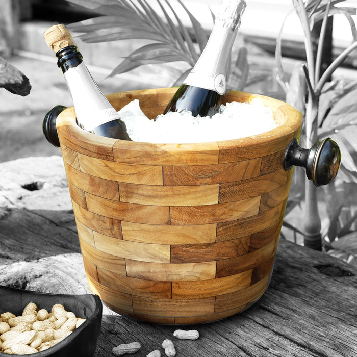 Rico & Plato angelia teak wine champagne ice bucket with ice and wine bottles inside next to a bowl of peanuts on a wooden surface outside