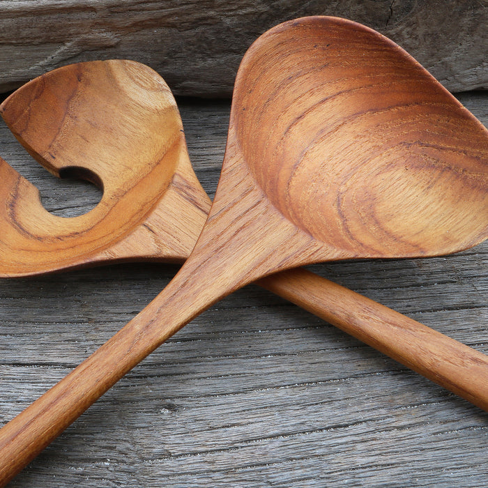 Close up of two teak salad serving utensils crisscrossed each other on a wooden surface