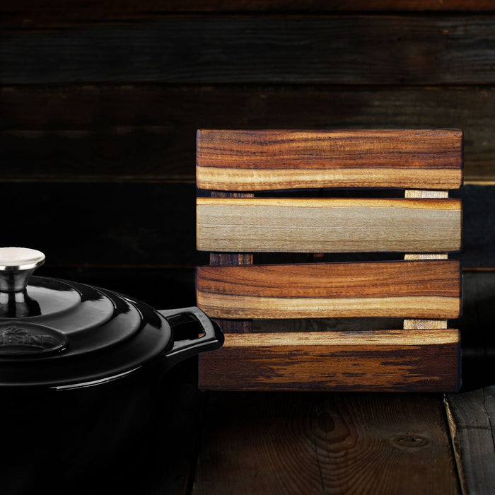 Teak trivet placed by a black pot displayed on a wooden surface