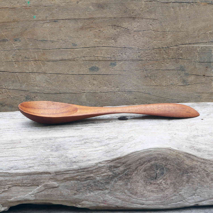 Side view of large teak spoon displayed on a wooden surface
