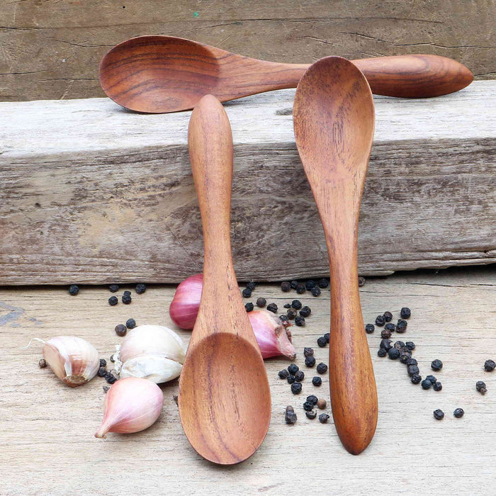 Set of 3 large teak spoons displayed on a wooden surface next to garlic and peppercorns