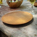 Teak wooden plate on a rustic wooden table with a glass of wine in the background
