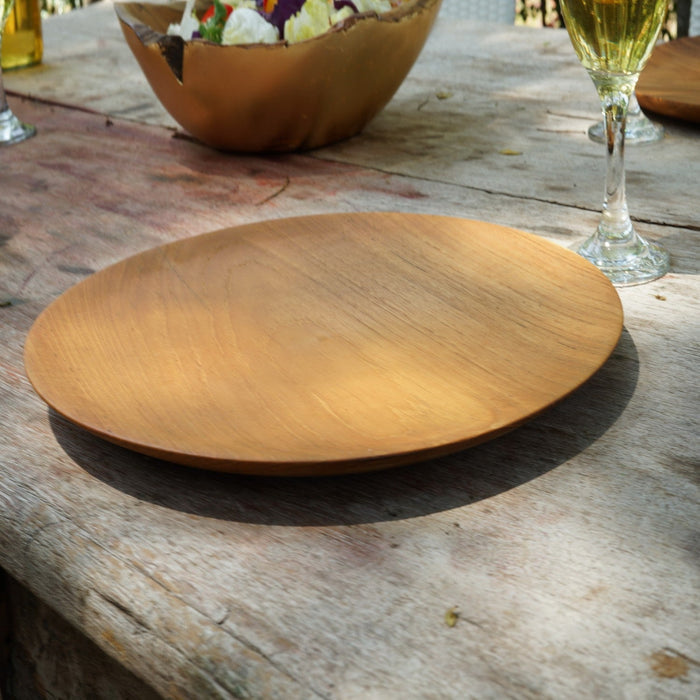 Teak wooden plate on a rustic wooden table with a glass of wine in the background