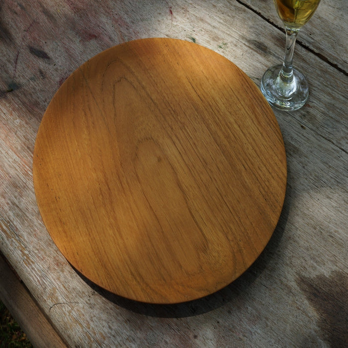 Top view of small teak plate next to a wine filled glass displayed on a wooden surface