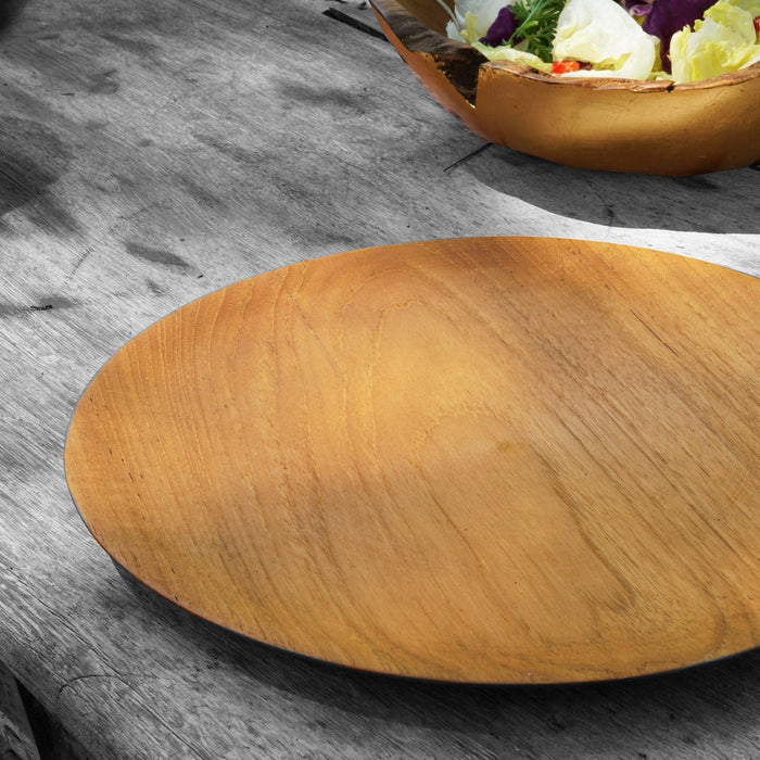 Small teak plate displayed on a wooden surface next to a wooden bowl with salad