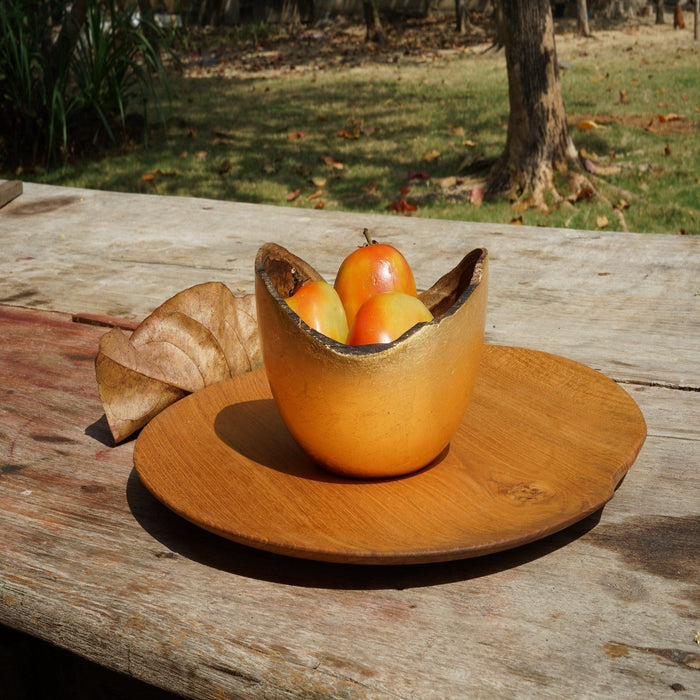 Small teak plate with a small bowl with fruit on top displayed outside on a wooden surface