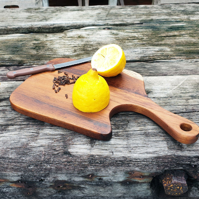 Rico & Plato teak cutting board/serving platter with sliced lemons and knife displayed on a wooden surface