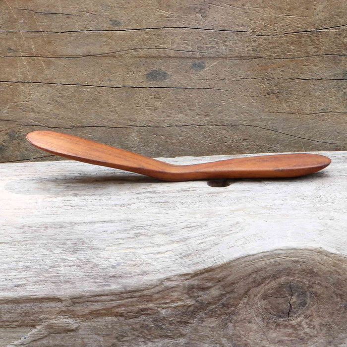 Side view of wooden butter spreader displayed on a wooden surface