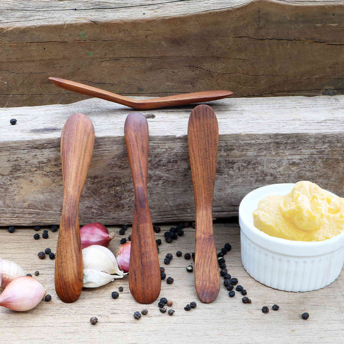 Set of 4 wooden butter spreader next to a bowl of butter, garlic, shallot, and peppercorn on a wooden surface