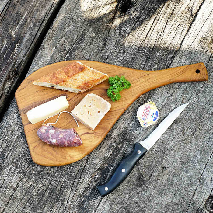 Rico & Plato caraway cutting board serving platter with cheese, sausage link, herb, and bread on top of platter next to a tub of butter and a knife displayed on a wooden surface