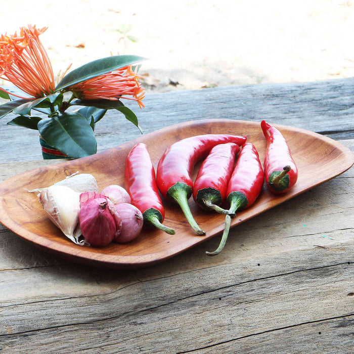 Small teak plate with garlic and chili peppers next to flowers displayed outside on a wooden surface