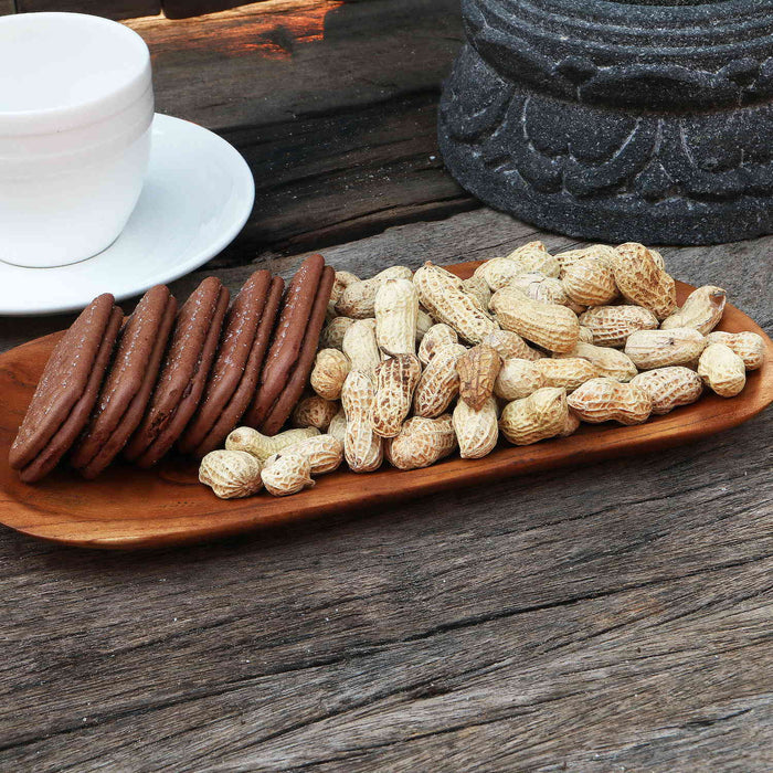 Small teak plate with peanuts and cookies displayed on a wooden surface