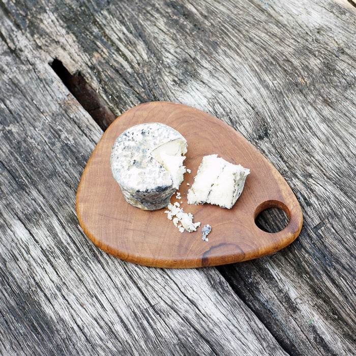 Teardrop styled teak cutting board with cheese displayed on a wooden surface