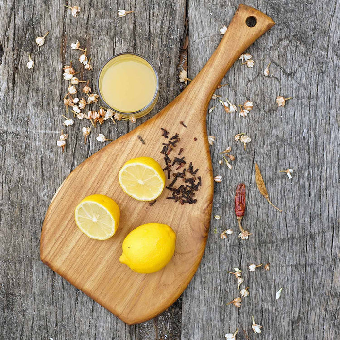 Top view of teak cutting board/serving platter with lemons and flowers displayed on a wooden surface