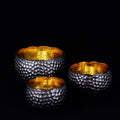 Three copper bowls with textured surfaces and black accent exterior on a black background