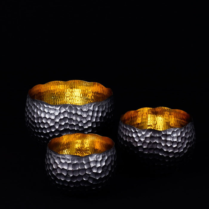 Three copper bowls with textured surfaces and black accent exterior on a black background