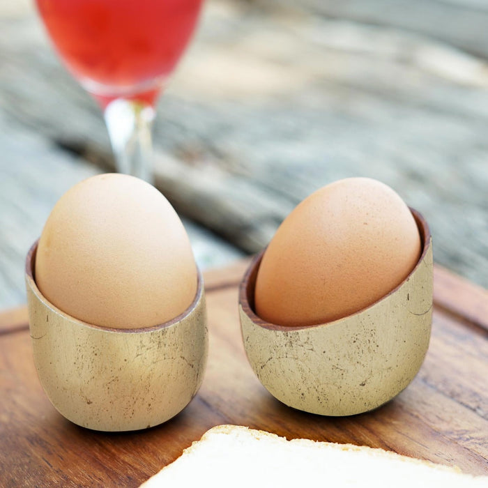 Set of 2 teak egg cup with gold leaf exterior with eggs inside placed on a wooden board