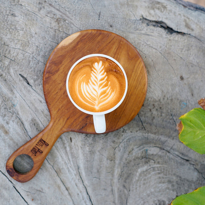 Top view of teak coffee cup server with a mug of creamy coffee displayed on a light gray background