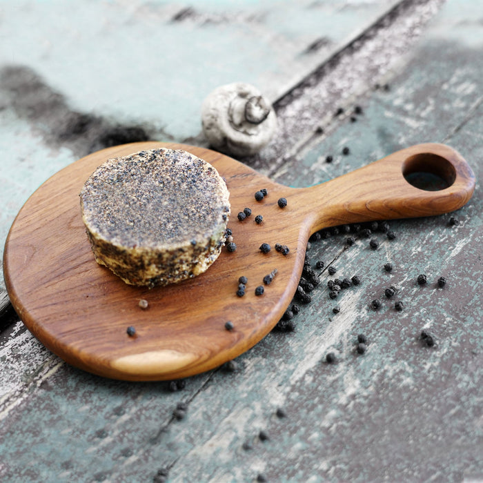Circular teak cutting board with cheese displayed on a wooden surface